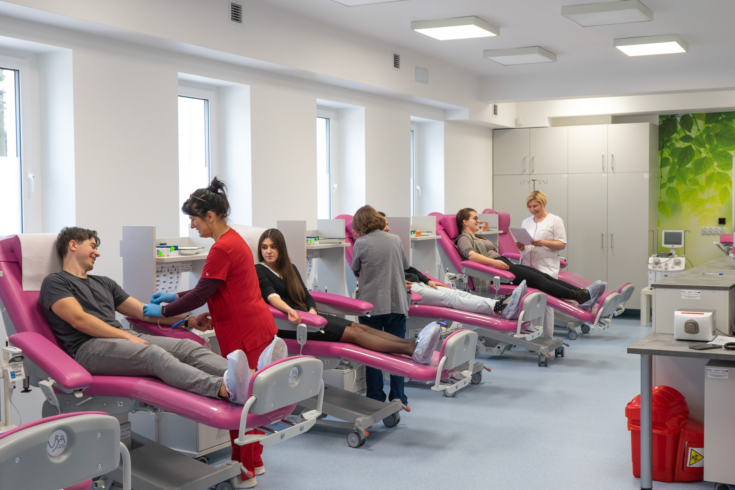 Zdjęcie przedstawia salę do pobierania krwi, gdzie znajdują się osoby oddające krew oraz personel medyczny