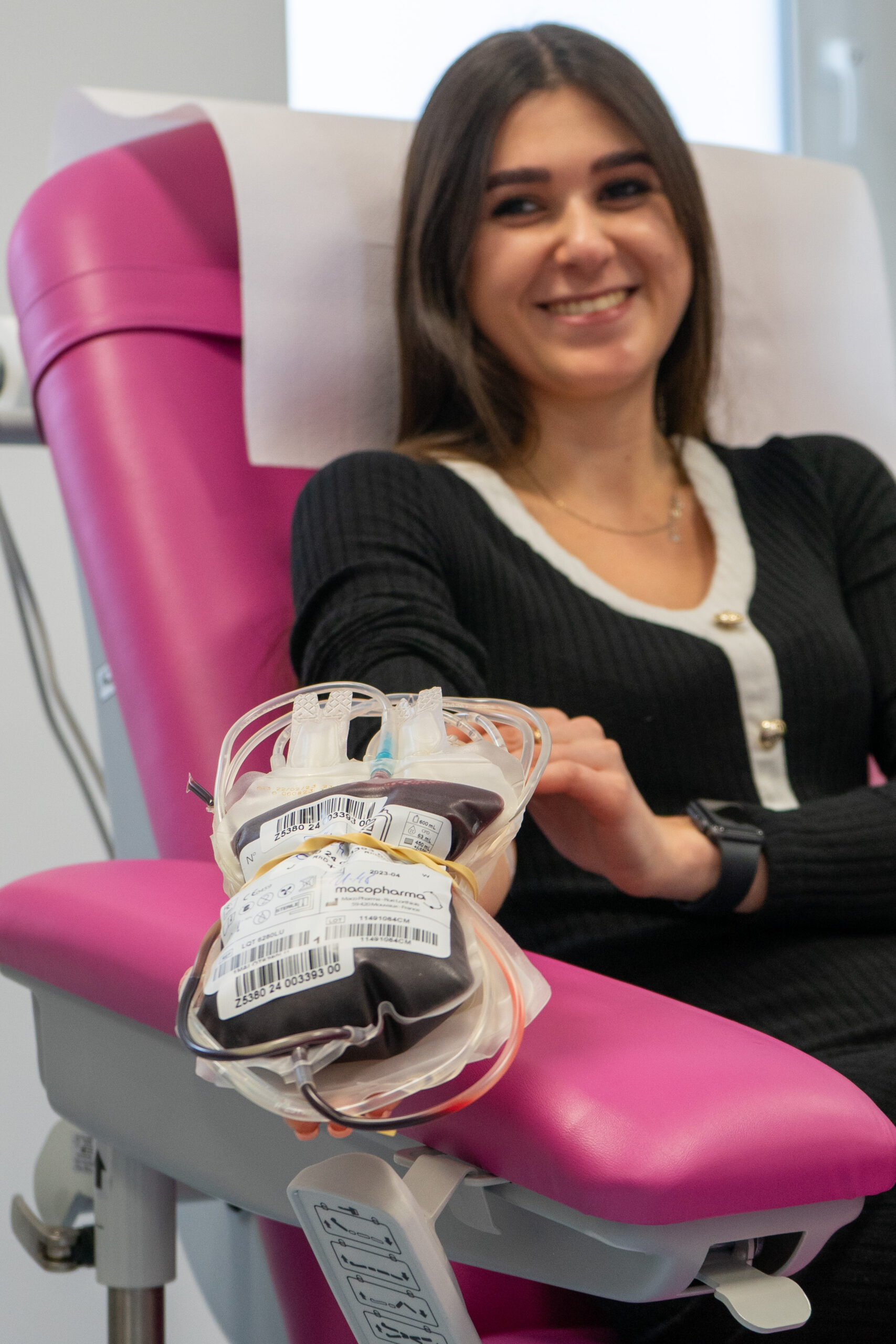 Kobieta trzymająca oddaną krew w ręku, siedząca na różowym fotelu w gabinecie do oddawania krwi.